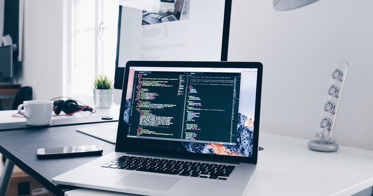 Un ordinateur portable ouvert sur un bureau clair, avec un écran secondaire, un casque et une tasse à côté.